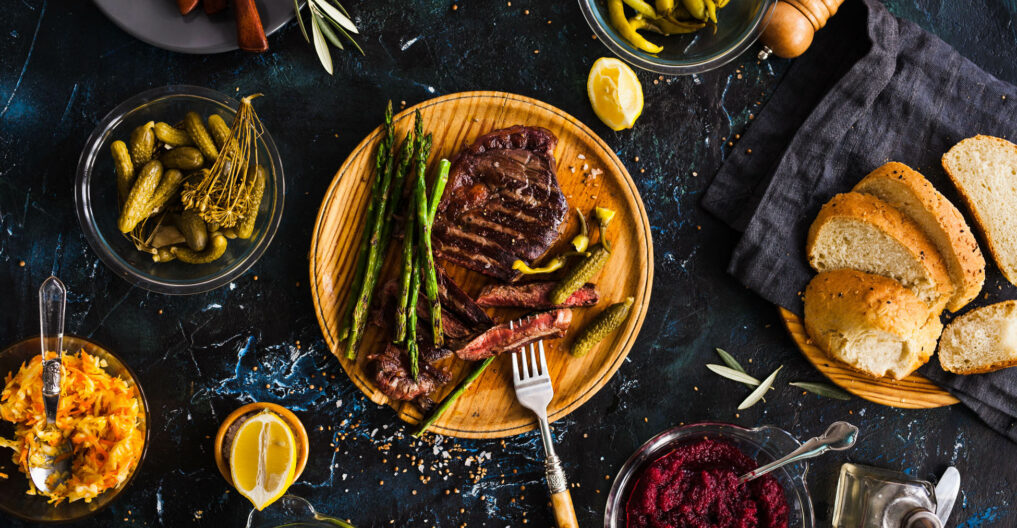 Grilled steak with asparagus and pickled peppers on a wooden plate.