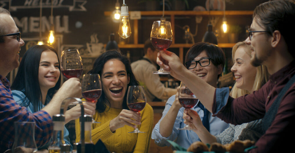 Friends joyfully clinking glasses over a meal in a cozy setting.