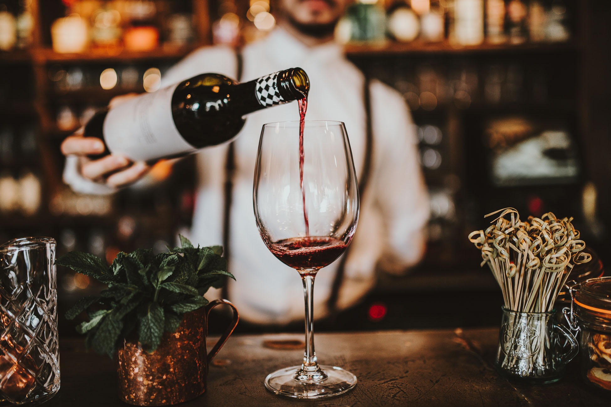 Pouring red wine into a glass at a cozy bar.