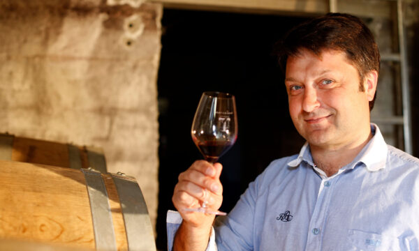 Man holding a glass of wine in a cellar with barrels.