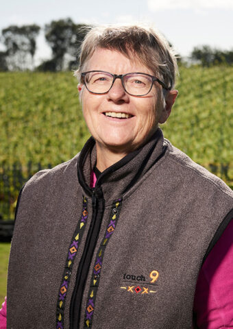 Smiling older woman wearing glasses and a fleece vest outdoors.