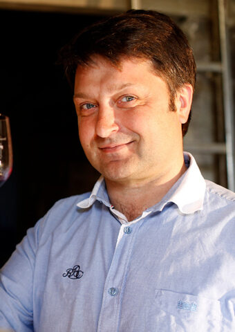 A man smiling warmly while holding a glass of red wine.