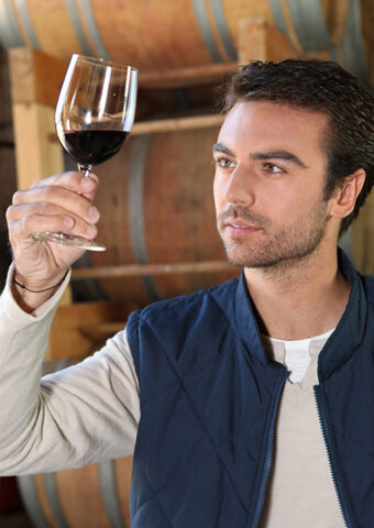 Man inspecting a glass of red wine in a rustic setting.