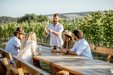 A man giving a presentation outdoors to a small group seated at a wooden table.